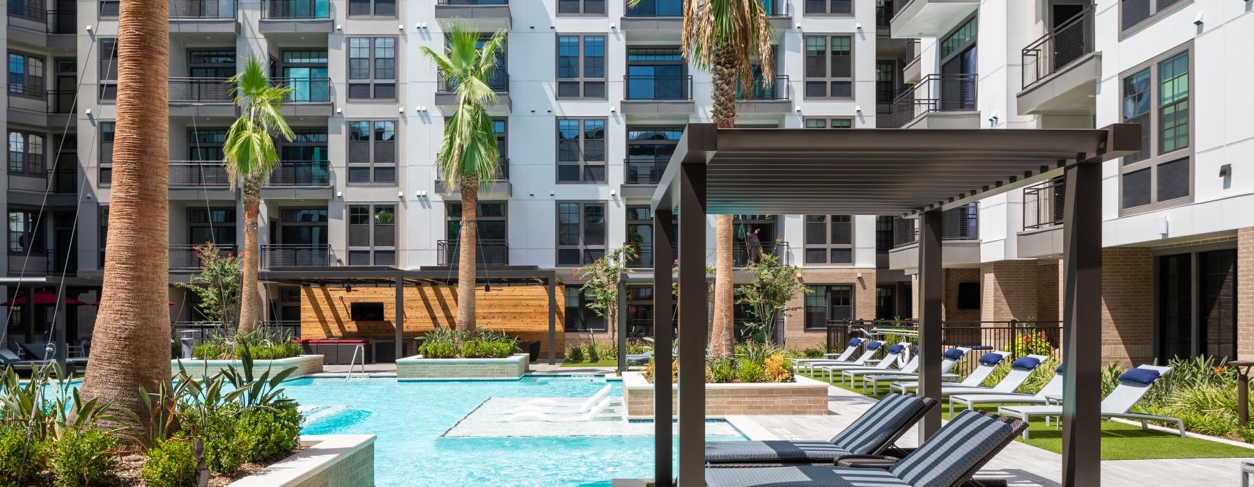 a pool in front of a building with lounge chairs and palm trees